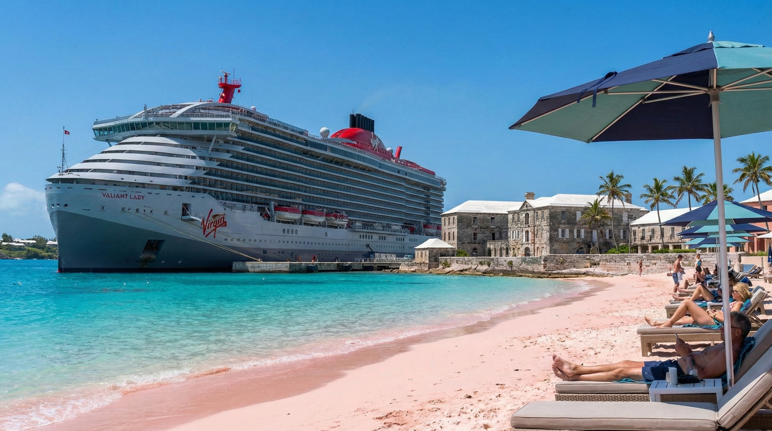 The Virgin Voyages Valiant Lady cruise ship docked at the Royal Naval Dockyard in Bermuda, with historic stone buildings, palm trees, and a pink sand beach under a clear blue sky.